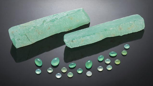 Figure 1. Two pieces of rough chrysoprase with several polished stones. The cabochons range from 0.77 to 2.15 ct. Photo by Nuttapol Kitdee; courtesy of John Wibberley, Chrysoprase Australia.