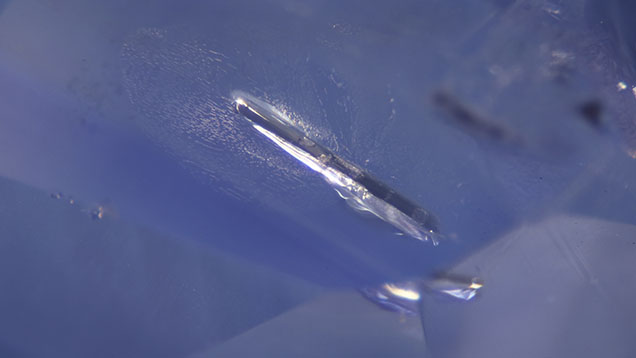 Elongated, rod-shaped vesuvianite crystal in sapphire associated with a partially healed fissure. Photomicrograph by Keith Chow; field of view 3.10 mm.