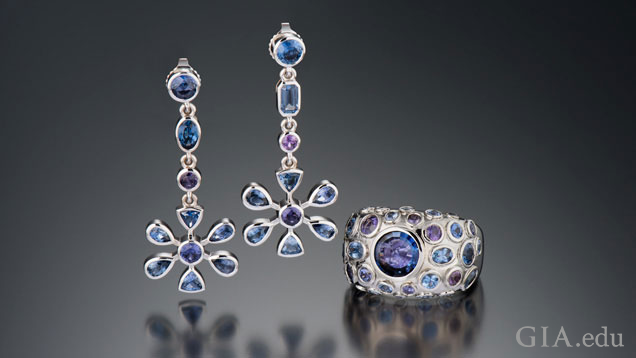 Earrings are flower-shaped and drop from a line of four blue and purple sapphires; the ring is domed-shaped with bezel-set blue and purple sapphires with a large blue center stone. Earrings are flower-shaped and drop from a line of four blue and purple sapphires; the ring is domed-shaped with bezel-set blue and purple sapphires with a large blue center stone.