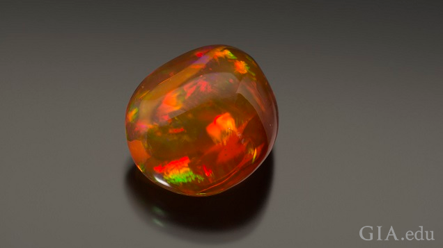 A polished gem with orange and green flashes of color.