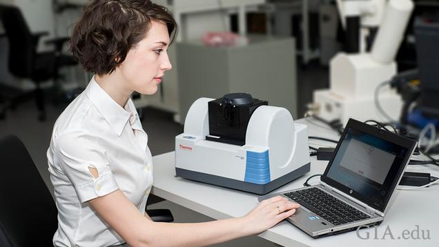 A woman sits in front of GIA’s Diamond Check machine and a computer. A woman sits in front of GIA’s Diamond Check machine and a computer.