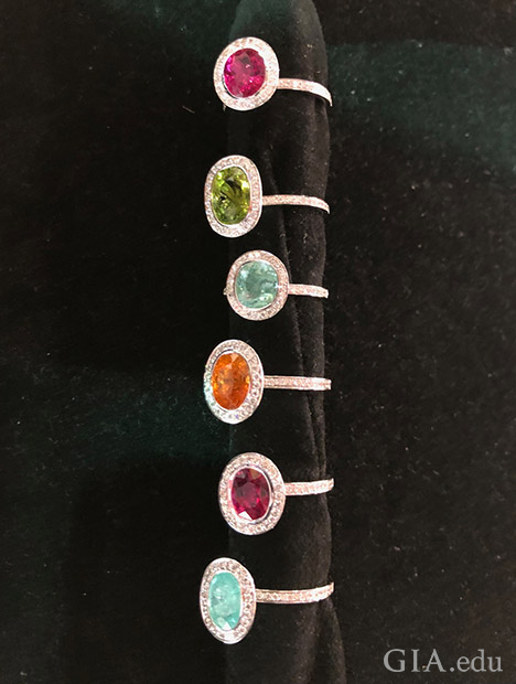 A column of six different colored tourmaline rings on a ring holder.