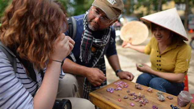 Manuel talks to two women as he looks at gems in a Vietnam gem market. The three sit around a small wooden table with gems separated into piles on it.