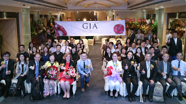 一大群人坐着拍照，纪念澳门分会的开幕庆典。 他们身后悬挂着 GIA 横幅。