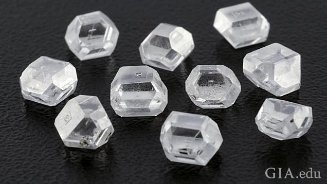 A group of 10 colorless rough crystals on a black background. A group of 10 colorless rough crystals on a black background.