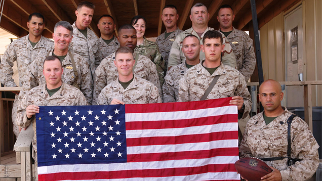 Diaz stands with 13 fellow Marines as they pose in camouflage with the American flag.