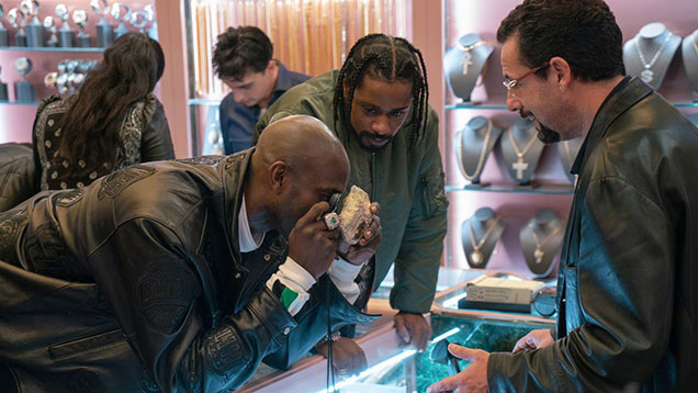 NBAの元スター選手、ケビン ガーネット(左)が、ジョシュ サファディとベニー サファディ監督による映画『Uncut Gems(邦題:アンカット・ダイヤモンド)』に本人役で出演し、レイキース スタンフィールド(中央)とアダム サンドラーと共演する。彼らは、サンドラーが演じるハワード ラトナーが劇中でオークションに出品するマトリックスに埋もれたエチオピア産オパールを見ている。写真提供:A24 Films(A24 フィルムズ) NBAの元スター選手、ケビン ガーネット(左)が、ジョシュ サファディとベニー サファディ監督による映画『Uncut Gems(邦題:アンカット・ダイヤモンド)』に本人役で出演し、レイキース スタンフィールド(中央)とアダム サンドラーと共演する。彼らは、サンドラーが演じるハワード ラトナーが劇中でオークションに出品するマトリックスに埋もれたエチオピア産オパールを見ている。写真提供:A24 Films(A24 フィルムズ)