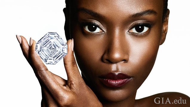 A model holds a large cut-corner square diamond with three fingers.