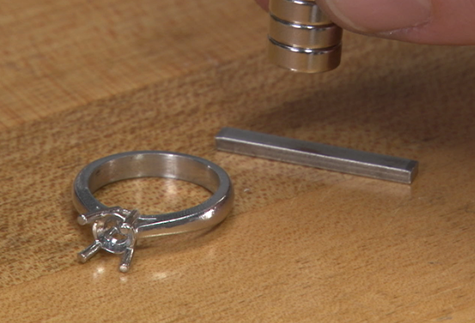 Solitaire ring setting without gemstone sitting next to a sizing wire with magnets above the wire Solitaire ring setting without gemstone sitting next to a sizing wire with magnets above the wire