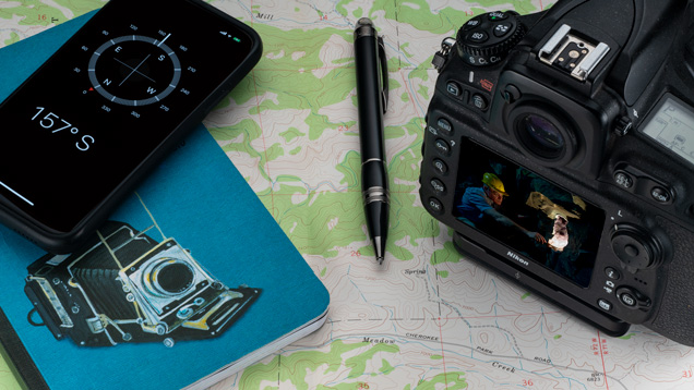 A notebook, pen, mobile phone with compass app and a digital camera sit on top of a map. A notebook, pen, mobile phone with compass app and a digital camera sit on top of a map.