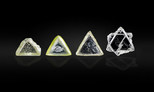 Figure 1. Examples of contact-twinned macle diamond crystals from South Africa. Left to right: a flat triangular macle with limited resorption (sample 11; 0.357 ct); an extensively resorbed variant of a flat triangular macle (sample 12; 0.411 ct); a very elongated flat macle with stacking growth layers on the octahedral faces, showcasing sharp edges and pointed apex corners (sample 13; 0.553 ct); a six-pointed star-shaped, poorly resorbed flat macle (sample 14; 0.747 ct). Photo by Tetsuya Chikayama; courtesy of Suwa & Son, Inc. Figure 1. Examples of contact-twinned macle diamond crystals from South Africa. Left to right: a flat triangular macle with limited resorption (sample 11; 0.357 ct); an extensively resorbed variant of a flat triangular macle (sample 12; 0.411 ct); a very elongated flat macle with stacking growth layers on the octahedral faces, showcasing sharp edges and pointed apex corners (sample 13; 0.553 ct); a six-pointed star-shaped, poorly resorbed flat macle (sample 14; 0.747 ct). Photo by Tetsuya Chikayama; courtesy of Suwa & Son, Inc.