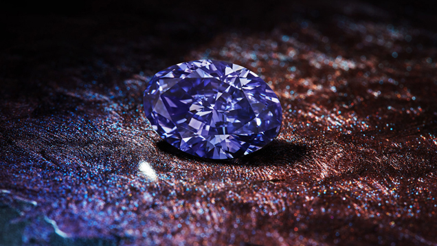 椭圆形的阿盖尔紫罗兰钻石 (Argyle Violet) 展示在带有纹理的棕色、紫色和蓝色表面之上。 椭圆形的阿盖尔紫罗兰钻石 (Argyle Violet) 展示在带有纹理的棕色、紫色和蓝色表面之上。
