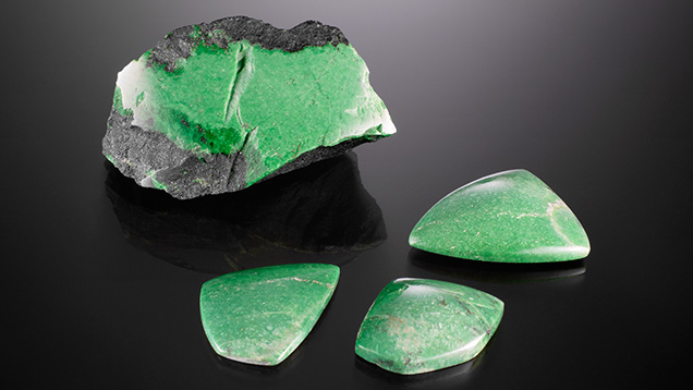 This 110.4 g partially polished rough grossular garnet “Transvaal jade” and three polished cabochons (41.95–92.87 ct) display unusually vibrant green colors between seams of dark chromite matrix. Photo by Diego Sanchez; courtesy of TMS Gems. This 110.4 g partially polished rough grossular garnet “Transvaal jade” and three polished cabochons (41.95–92.87 ct) display unusually vibrant green colors between seams of dark chromite matrix. Photo by Diego Sanchez; courtesy of TMS Gems.