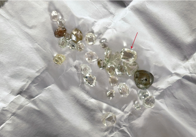 Figure 3. A parcel of rough diamonds, collected over a month by a Liberian artisanal miner. The diamond indicated by the arrow weighs 0.80 ct. Photo by Beth West. Figure 3. A parcel of rough diamonds, collected over a month by a Liberian artisanal miner. The diamond indicated by the arrow weighs 0.80 ct. Photo by Beth West.
