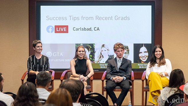 Four speakers sit on a stage in front of an audience.