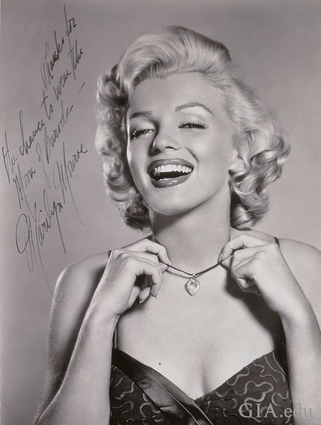 A black and white photo of a smiling Marilyn Monroe wearing the Moon of Baroda. It is signed: “Thanks for the chance to wear the Moon of Baroda – Marilyn Monroe”