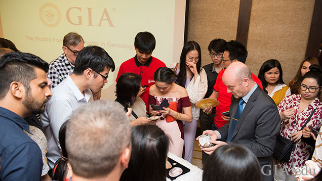 More than a dozen people surround a table of pearl and mollusk samples.