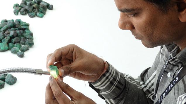 A worker uses a light to sort through several piles of rough emeralds.
