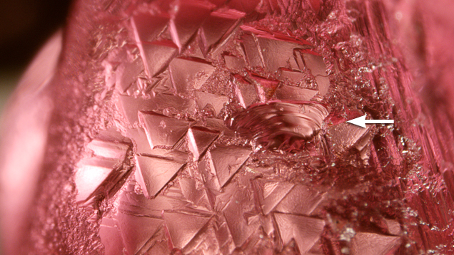 In addition to trigons, the spinel displayed a conchoidal fracture (see arrow), a feature not found in diamond. Magnified 40x.