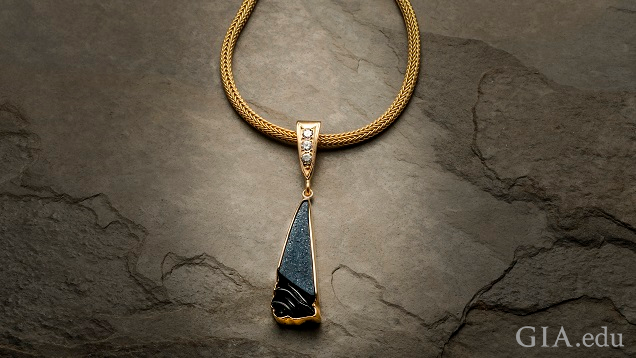 一件三角形的黑色条纹玛瑙晶簇雕刻品，周围镶嵌着一圈 14k 黄金。它挂在黄金链的一个三角形黄金夹件上，并镶有三颗 0.10 分的钻石。