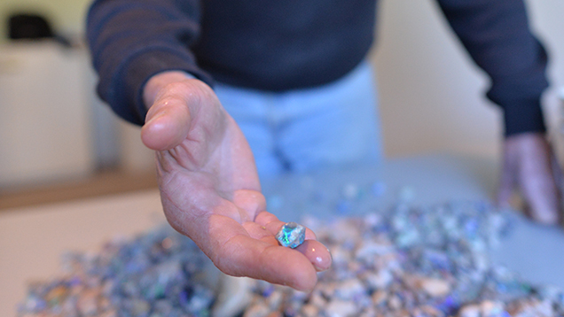 Man showing a piece of rough opal from a pile of stones