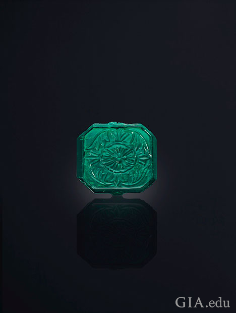 A square shaped emerald with carving on top. A square shaped emerald with carving on top.