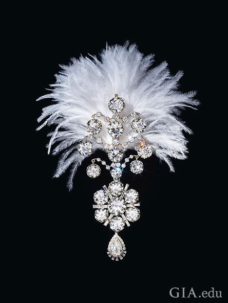 A diamond brooch topped with a white feather plume. A diamond brooch topped with a white feather plume.