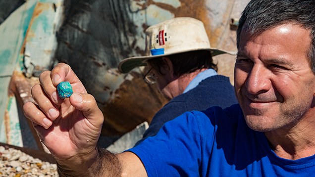 Man holding black opal. 那天我们走访了蛋白石处理区，Frederic Mallock（弗雷德里克·马洛克）正在处理几天的矿产，我们在场观察时，他发现了一块引人注目的黑色蛋白石。 摄影：Andrew Lucas（安德鲁·卢卡斯）/GIA。