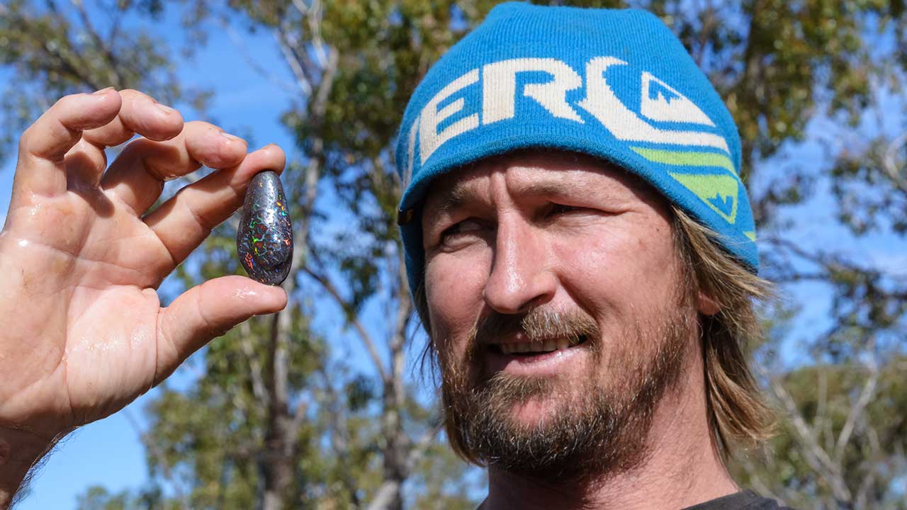 DSC_2612-185754-1280x720.jpg. Boulder opal miner Mark Moore displays one of the boulder opals showing seams of color in the dark ironstone matrix he cut from his mine’s production at Koroit. Photo by Andrew Lucas/GIA.