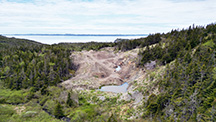 alt="Figure 2. View of the amethyst-bearing trench looking west-southwest into Placentia Bay. The vein is exposed in the right side of the trench, and overburden is displaced to the left. Aerial drone photo by Philippe Belley."