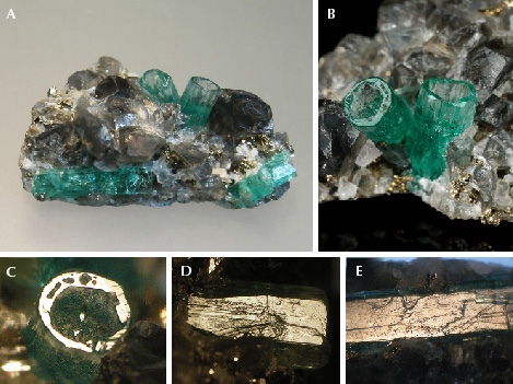 Figure 17. A: In sample 17 (26 mm long), a base of black shale (not visible) is covered with albite, calcite, and pyrite crystals. In this matrix, five emerald crystals are embedded, two of them as deep cups (center) and three as “normal” emeralds (lower right and left). B: Details of the two emerald cups (5.5 mm long on the right). C: In reflected light, the basal plane of one cup appears bright together with the basal faces of small hillocks or columns in the cup. D: Growth steps on the surface of one m prism face of a cup. E: Growth steps on the surface of the m prism face of a “normal” emerald crystal. Photos by K. Schmetzer (A, C–E) and G. Martayan (B); field of view 7.6 mm (C–E).