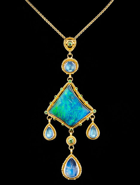 Figure 2. “Where the Ocean Meets the Sky” is a one-of-a-kind pendant featuring a 19.51 ct Australian boulder opal and 11.37 carats of blue moonstone. The boulder opal is accented with 0.63 carats of tsavorite garnet. The granulated yellow gold is 22K, and the gold links between the elements are 18K yellow gold. Photo by Robert Weldon; courtesy of Zaffiro. Figure 2. “Where the Ocean Meets the Sky” is a one-of-a-kind pendant featuring a 19.51 ct Australian boulder opal and 11.37 carats of blue moonstone. The boulder opal is accented with 0.63 carats of tsavorite garnet. The granulated yellow gold is 22K, and the gold links between the elements are 18K yellow gold. Photo by Robert Weldon; courtesy of Zaffiro.