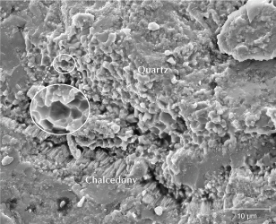 Figure 18. An SEM image of sample S3 reveals well-formed quartz particles approximately 5 μm in diameter, with a hexagonal cross section left by a fracture. Fibrous chalcedony is observed at the border transition. Figure 18. An SEM image of sample S3 reveals well-formed quartz particles approximately 5 μm in diameter, with a hexagonal cross section left by a fracture. Fibrous chalcedony is observed at the border transition.