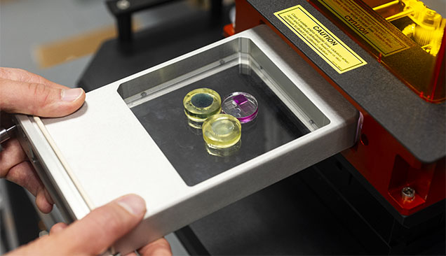 Figure 4. LA-ICP-MS analyses are standardized with NIST glass standard reference material (the blue and colorless pieces in yellow epoxy) for a variety of elements. Also shown is our internally developed matrix-matched corundum standard (colorless epoxy with four variously colored sapphires) used specifically for ruby and sapphire analysis. Photo by Kevin Schumacher. Figure 4. LA-ICP-MS analyses are standardized with NIST glass standard reference material (the blue and colorless pieces in yellow epoxy) for a variety of elements. Also shown is our internally developed matrix-matched corundum standard (colorless epoxy with four variously colored sapphires) used specifically for ruby and sapphire analysis. Photo by Kevin Schumacher.