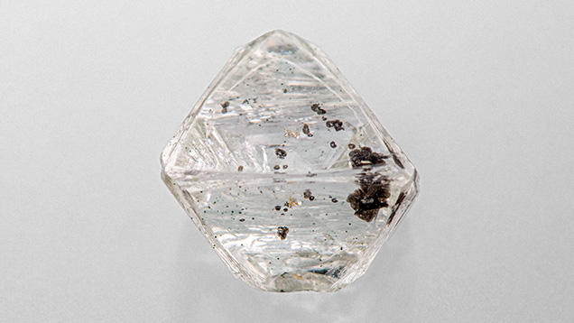 Figure 1. Weighing 2.34 ct and measuring 7.71 mm in the largest dimension, this partially etched diamond octahedron hosts a yellow-orange almandine-pyrope garnet crystal. Photo by Diego Sanchez.