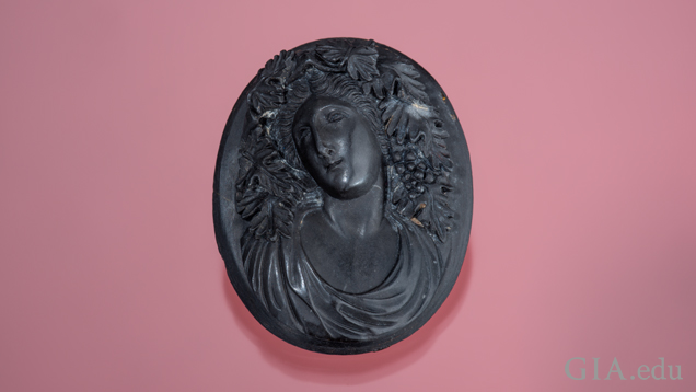 The goddess Bacchante is carved in high relief in black lava and shows fine detail of leaves and clusters of grapes in her hair.