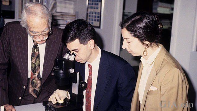 Two men and a woman gather around a microscope.