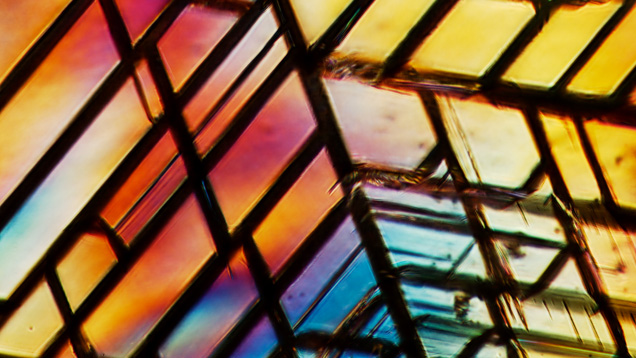 Between crossed polars the diamond shows high-order interference colors consistent with the strain causing the cleavage network along the octahedral planes. Photomicrograph by Jonathan Muyal; field of view 0.62 mm.