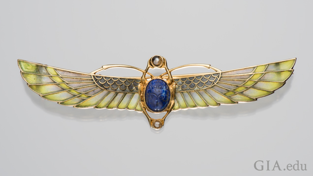 A scarab brooch with two sets of wings – one set is short, the other elongated. The body is a lapis lazuli and the long wings are a blue-green enamel.