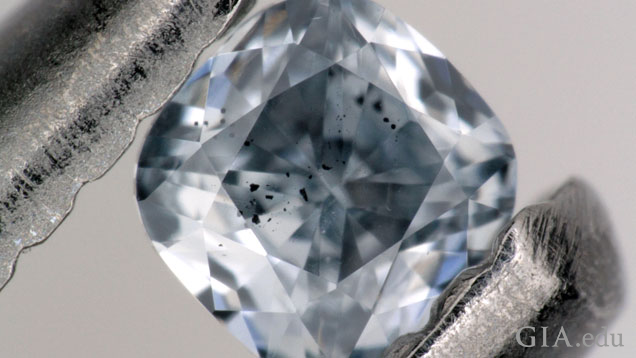 A blue diamond with inclusions under the table is held up in tweezers.