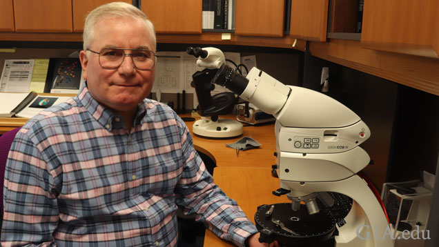 Man sits next to microscope.