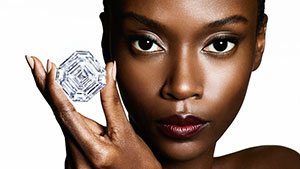 A model holds a large cut-corner square diamond with three fingers.