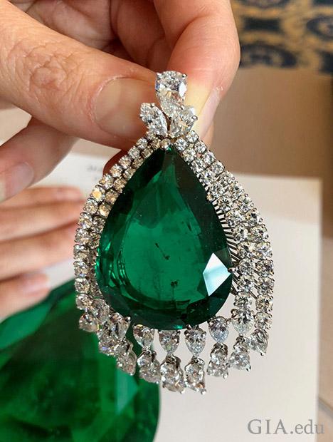 A pear shaped emerald framed by two rows of various sized diamonds.