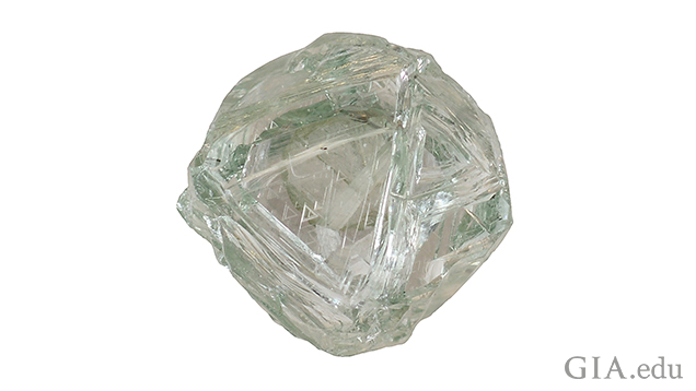 A piece of diamond rough with green body color and triangular etchings on the surface.