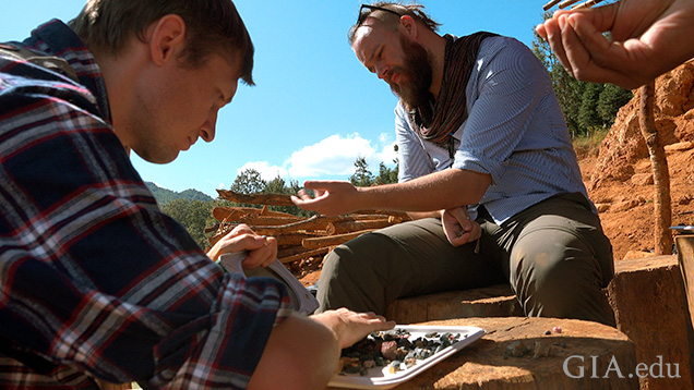 Two men sort through gem gravel on site.