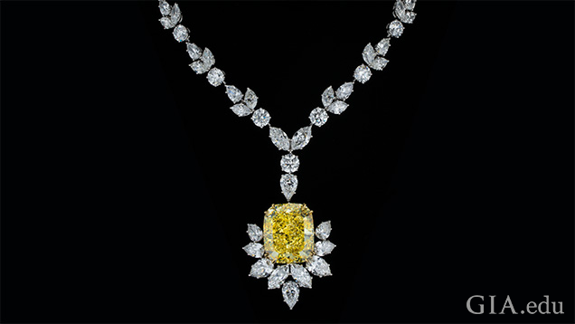 A large yellow cushion cut diamond pendant is partially framed with marquis cut diamonds and hangs from a necklace of mixed cut diamonds.  