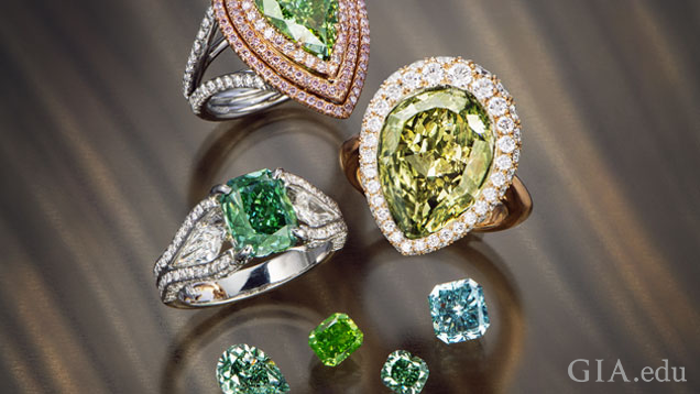 Three beautiful rings are clustered near four loose diamonds. All pieces include green diamonds of different shades.