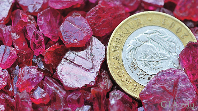 A pile of rough of rubies with a coin for perspective.