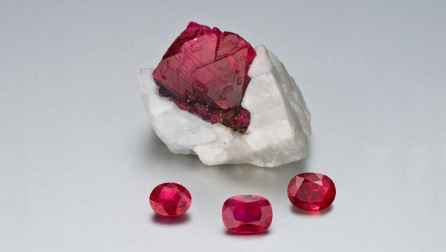 A large ruby crystal in calcite with three faceted rubies in front. 