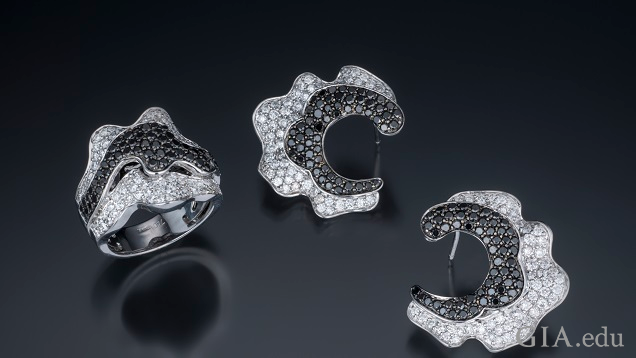 The ring is designed with a wavy strip of black diamonds in the centre framed on each side with colourless diamonds set in a ruffled edge. The earrings are crescent shaped with black diamond on the inside framed by colourless diamonds in a ruffled edge.